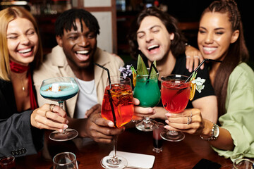 A joyous group of young colleagues raises colorful cocktails, celebrating their success at a party.