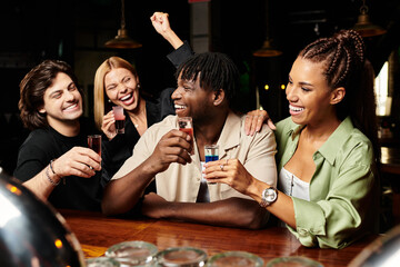 A cheerful group of young professionals enjoys shots and laughter during a corporate celebration.