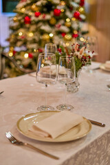 Christmas festive modern restaurant interior with greenery, pleasant cozy lighting and festive table setting with glasses.