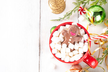 Naklejka premium Funny Christmas hot chocolate with marshmallow and chocolate gingerbread man taking chocolate bath in red mug, on festive holiday decorated background