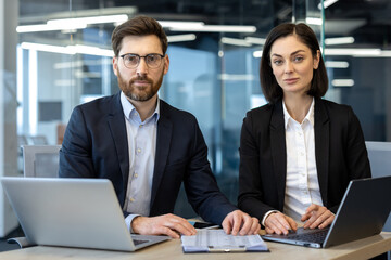Business professionals sitting in office with laptops looking confident. Teamwork concept featuring modern technology, collaboration, and productivity in corporate environment.