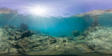 A serene underwater scene with sunbeams penetrating the surface, lighting up the rocky ocean floor in a 360-degree view. The peaceful underwater environment is calm and still.