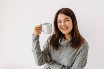 Happy asian woman holding and showing white cup with smiling face in winter, drinking hot water coffee, making warm, isolated over white background wall.