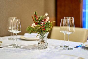 Christmas festive modern restaurant interior with greenery, pleasant cozy lighting and festive table setting with glasses.
