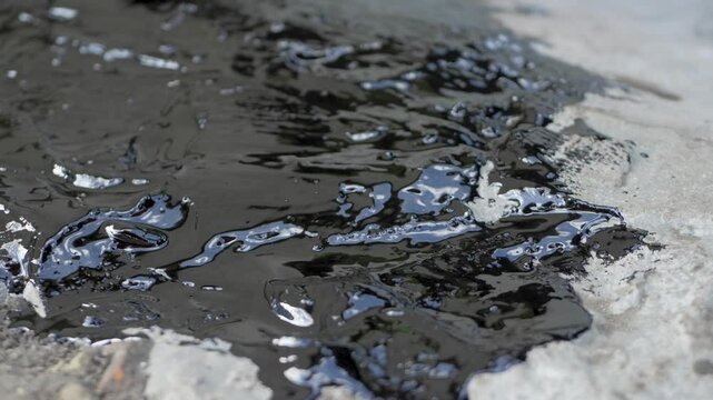 Gloved hand uses a brush to spread waterproofing putty on concrete. This putty protects buildings from water, sealing cracks and creating a moisture barrier