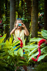 View of an 8-year-old girl standing among blooming red ginger flowers with her mouth open due to...