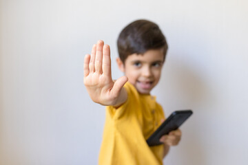 Cute little boy with mobile telephone show stop gesture, close up. Say no, whims, emotions and facial expression.