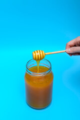 Płynny miód nabrany na drewnianą łyżkę ściekający z powrotem do słoika