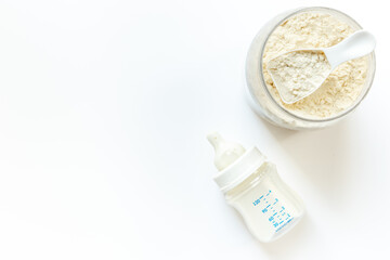 Jar of powdered milk for baby food with bottle of milk and spoon, top view