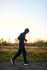 Young guy jogging early in the morning in the park in black sportswear
