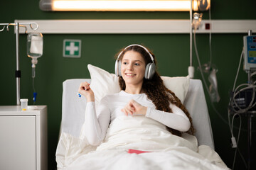 Enjoying music, the patient wears headphones in her comfy bed in hospital ward.