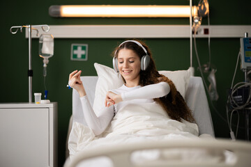 Resting in the ward, female patient listens to music with headphones.