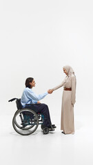 Obraz premium Man in wheelchair shaking hands with Muslim woman in beige dress, showcasing mutual respect and inclusion in professional setting. Concept of business, dei, equality, support