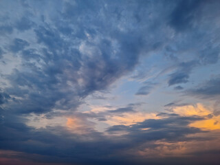A vast sky view with dynamic clouds formation, hues of blue and subtle orange at the horizon, suggesting either sunrise or sunset. The interplay of light and cloudscape creates a serene atmosphere