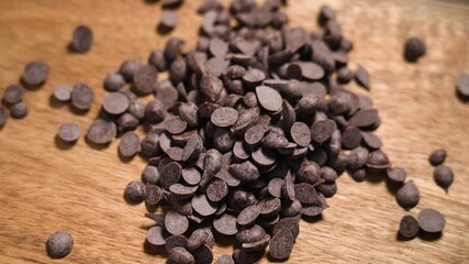 Organic pure chocolate chips falling on eco friendly rustic wooden surface in slow motion close up. Sweet bake pieces. Top view - Powered by Adobe
