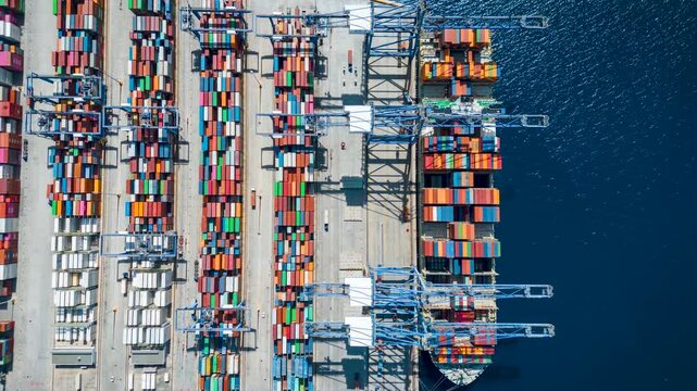 Aerial overhead time lapse view of  large container cargo ship being unloaded by cranes and trucks in a commercial terminal port