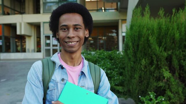 Portrait of young smiling Latin American non binary Gen Z student standing outside at college campus. Joyful man with backpack looking at camera outdoor. Education and university lifestyle concept.