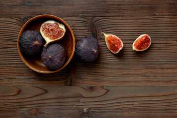 Fresh ripe figs in a wooden bowl on dark wooden table, top view