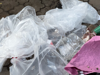 A pile of plastic bags and plastic wrap on the ground. The bags are white and the wrap is clear. The scene is messy and disorganized