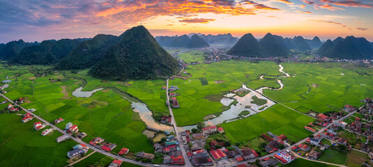 Colorful sunset over Bac Son Valley with mountains, lush green fields, winding river and village in Vietnam