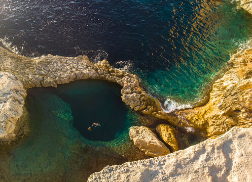 people swimming in blue hole Natural pool on the cliff in triq id dwejra in Gozo Malta of the Mediterranean coast with turquoise blue waters 