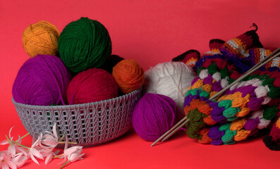 A Piece of knitting with color threads ball of yarn and a knitting needle on red background.