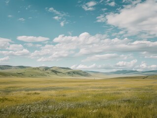 Naklejka premium Rolling hills and expansive grasslands stretch out under a clear blue sky filled with white clouds, showcasing a serene natural beauty