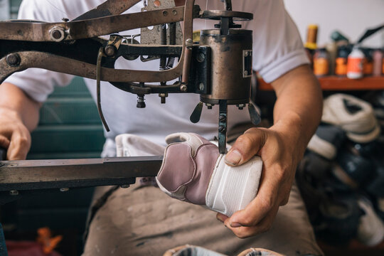 The hands of a shoemaker sewing the bottom of a sneaker
