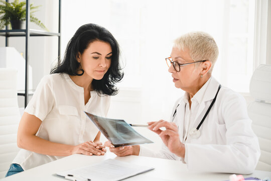 Radiogram. Caucasian senior female doctor general practitioner showing x-ray lungs photo to female patient, explaining diagnosis, symptoms at hospital