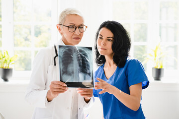 Two female doctors nurses interns caregivers checking discussing diagnosis on x-ray photo of lungs...