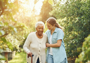 Young woman volunteer assisting happy senior woman with walking stick in a garden - Powered by Adobe