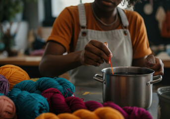 Textile artist is preparing a dye bath in a stainless steel pot, surrounded by colorful yarn balls, in her vibrant workshop