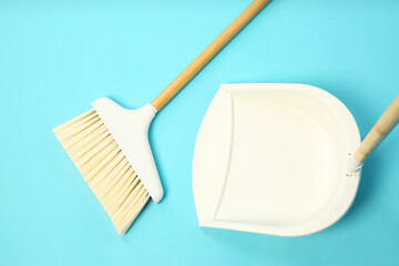 Cleaning broom and dustpan on light blue background, flat lay