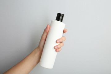 Woman with shampoo bottle on grey background, closeup