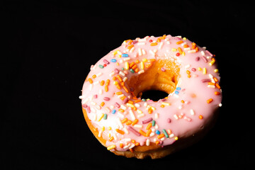 Pink frosting donut with sprinkles on black background 