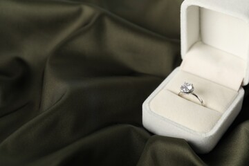 Beautiful ring with gemstone in box on black fabric, closeup. Space for text
