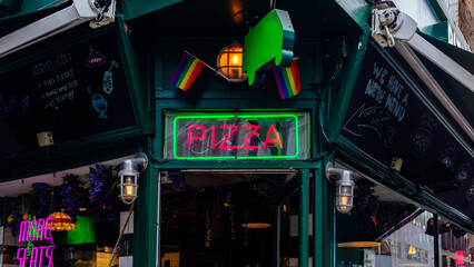 Restaurant facade displaying a neon pizza sign and rainbow flags