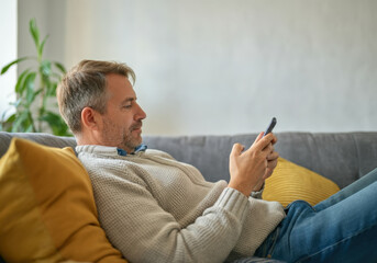 Man is relaxing on his sofa, browsing on his smartphone