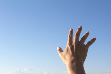 A shadowy male hand reaches out against the blue sky.