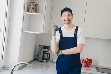Smiling handyman in uniform performs home repair in modern kitchen with confidence and skill