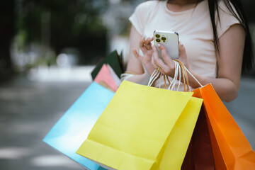 A cheerful young Asian woman holds shopping bags with a bright smile, excited by her summer...