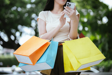 A cheerful young Asian woman holds shopping bags with a bright smile, excited by her summer...