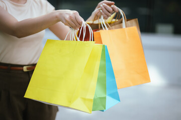 A beautiful young Asian woman walks happily through a city mall, holding shopping bags from her...