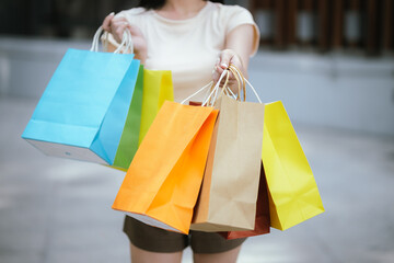 A beautiful young Asian woman walks happily through a city mall, holding shopping bags from her...