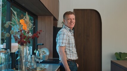 Happy old grandfather confidently standing pose while look at camera for good event or anniversary in kitchen. Cheerful senior enjoy retirement life with beautiful kitchenware and house. Divergence.