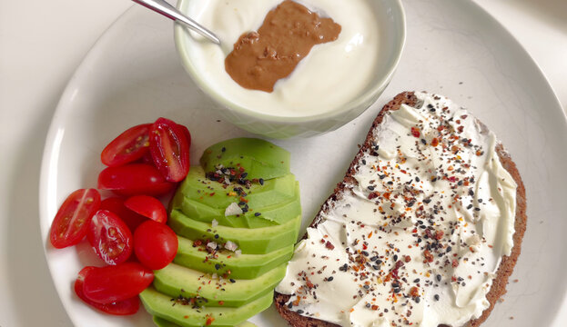 Fr&uuml;hst&uuml;cksteller mit Joghurt, Nussmuss, Vollkornbrot, Avocado und Tomate