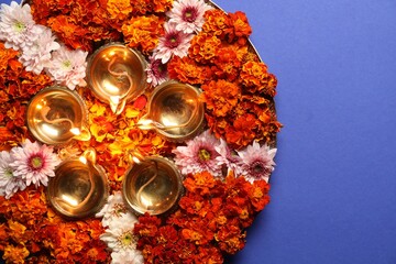 Diwali celebration. Diya lamps and beautiful flowers on blue background, top view