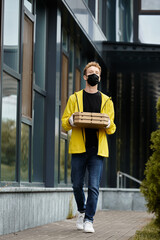 A delivery man in a medical mask is carrying pizza boxes into a bustling office building.
