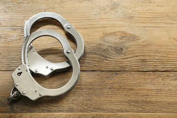 Classic chain handcuffs on wooden table, closeup. Space for text