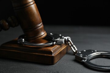 Handcuffs and judge's gavel on black wooden table, closeup
